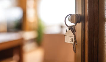 House-shaped keys are hanging from the door knob of a new home, representing the exciting moment of acquiring property and starting a fresh chapter