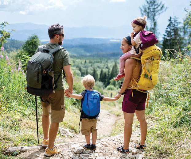 Rear view of family with small children hiking outdoors in summer nature, standing and resting.