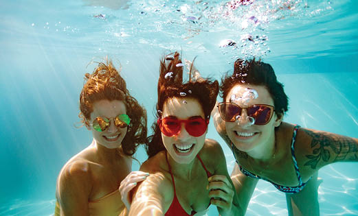 Cheerful women friends swimming underwater in pool taking selfie. Underwater selfie of happy females in pool.