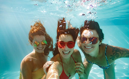 Cheerful women friends swimming underwater in pool taking selfie. Underwater selfie of happy females in pool.