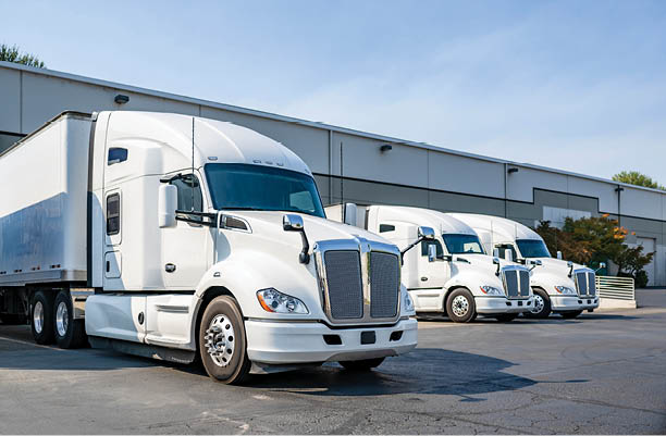 Industrial long hauler carriers white big rig semi trucks tractors with high cab for truck driver rest standing on the parking lot in warehouse docks gates loading cargo for the next delivery freight
