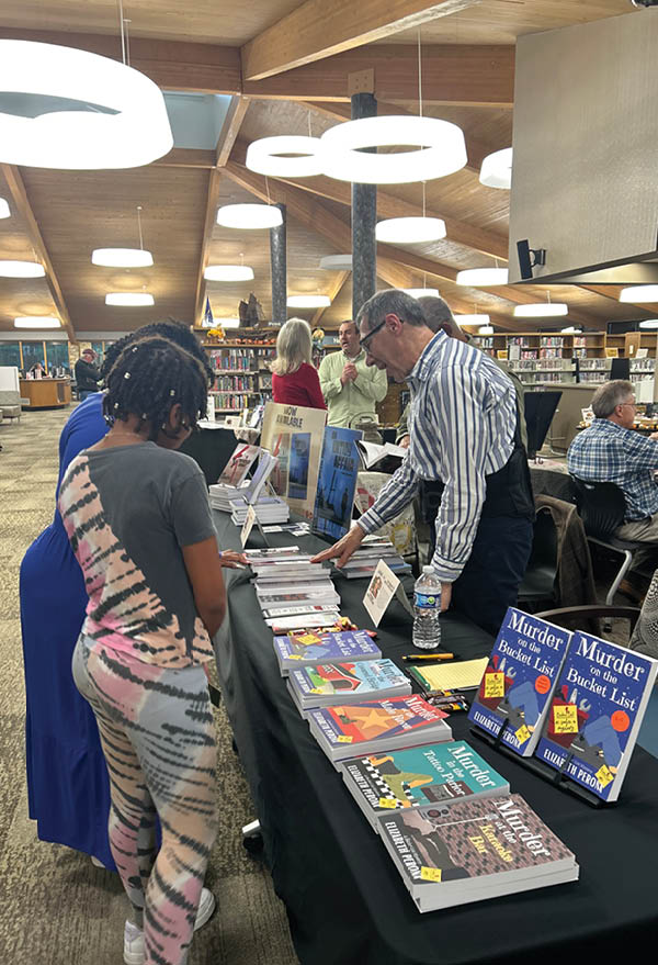 A woman in a black and white striped shirt is looking at a table with books on it. Description generated by AI