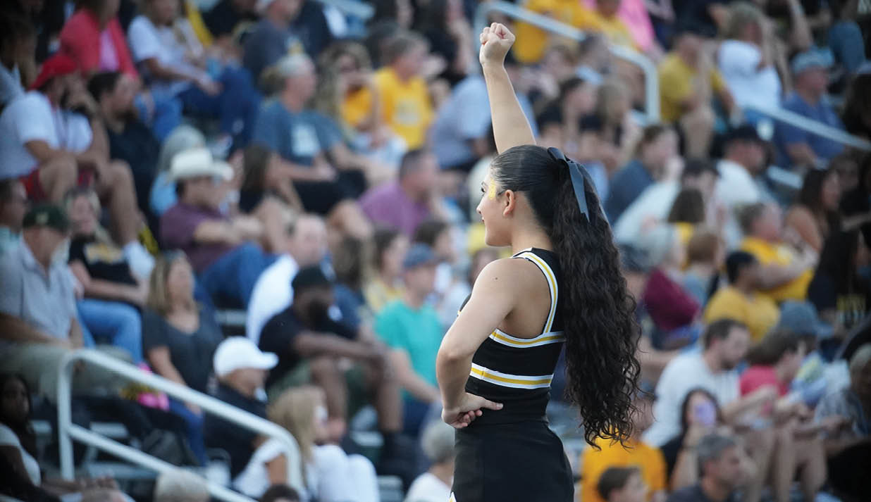 A woman wearing a black and yellow outfit stands on a field with her arms raised. Description generated by AI