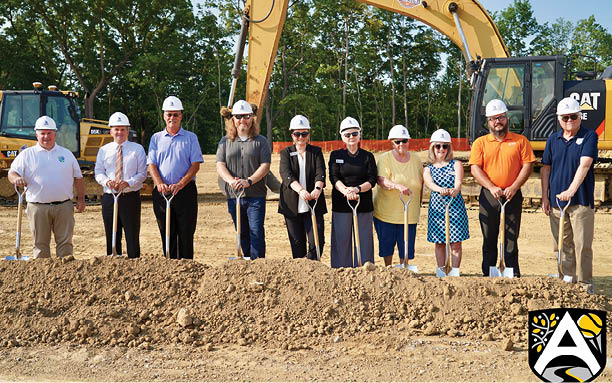 A group of people are standing in a dirt field, holding shovels. Description generated by AI