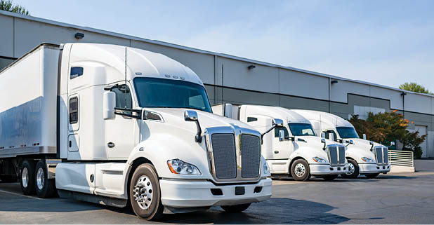 Industrial long hauler carriers white big rig semi trucks tractors with high cab for truck driver rest standing on the parking lot in warehouse docks gates loading cargo for the next delivery freight