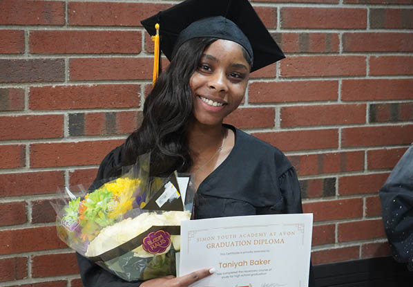 A woman in a graduation cap and gown holding a bouquet of flowers. Description generated by AI
