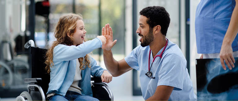 Young multiracial doctor having fun with little girl on a wheelchair.
