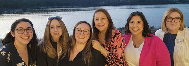 A group of six women posing for a picture in front of a body of water. AI generated content