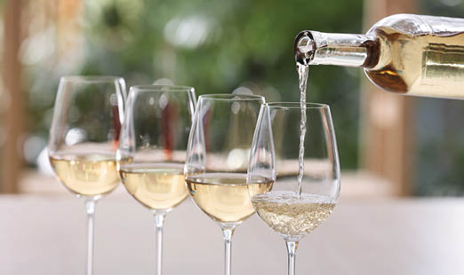Pouring white wine from bottle into glass on blurred background
