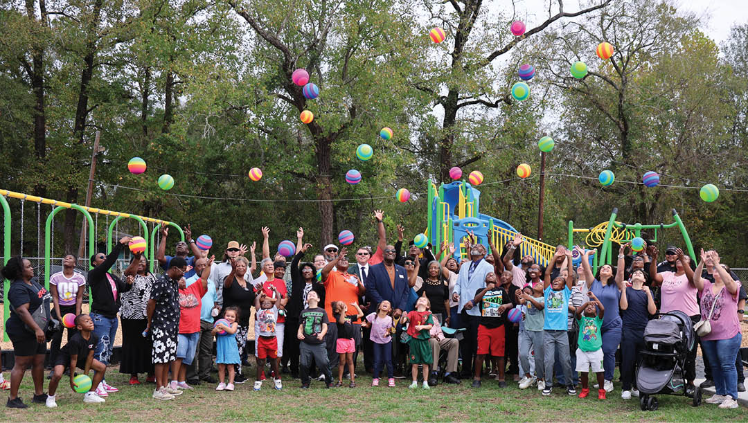 A group of people, including children, are gathered in a park. They are holding up balloons and playing with them. AI generated content