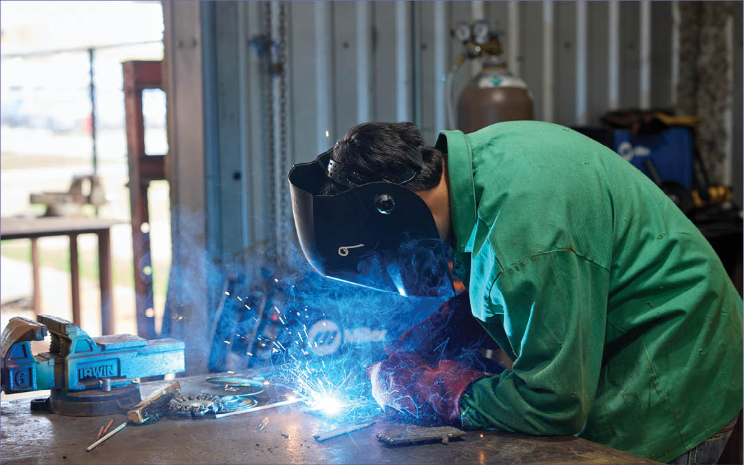 A man wearing a green shirt is working on a metal object, using a welding torch. AI generated content