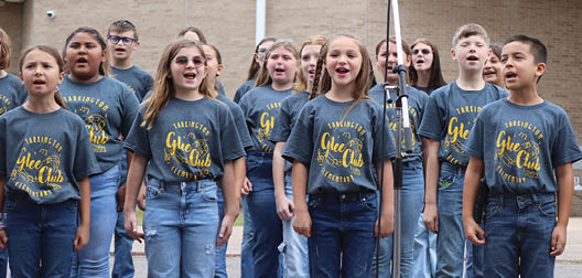 A group of children wearing blue jeans and grey shirts are singing together. AI generated content