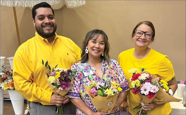 Three people are standing in front of a table with flowers. AI generated content