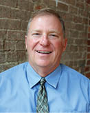 A man wearing a blue shirt and a green tie is smiling for the camera. AI generated content