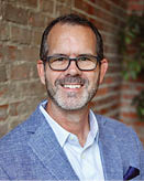 A man wearing a blue jacket and glasses is smiling. AI generated content