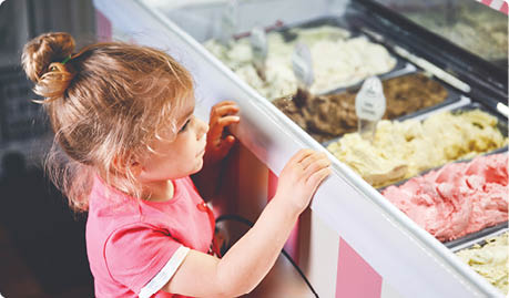 Cute little toddler girl choosing and buying ice cream in a cafe. Happy baby child looking at different sorts of icecream. Sweet home made dessert.