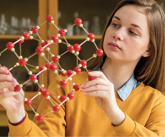 Female student holding molecular structure model. Science class concept.