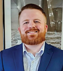 A man wearing a blue suit and a white shirt with a patterned design is smiling for the camera. AI generated content