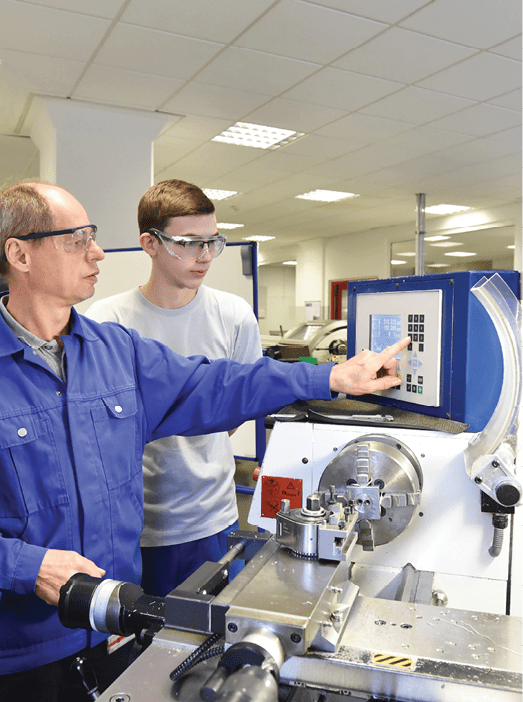 young apprentices in technical vocational training are taught by older trainers on a cnc lathes machine