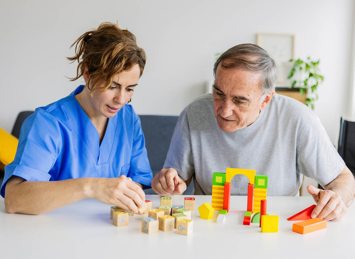 Female caregiver and senior man playing wooden shape puzzles game for dementia prevention