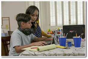 A mom working from home and sharing a small space with her children who are attending school via virtual classrooms stops to help her son 