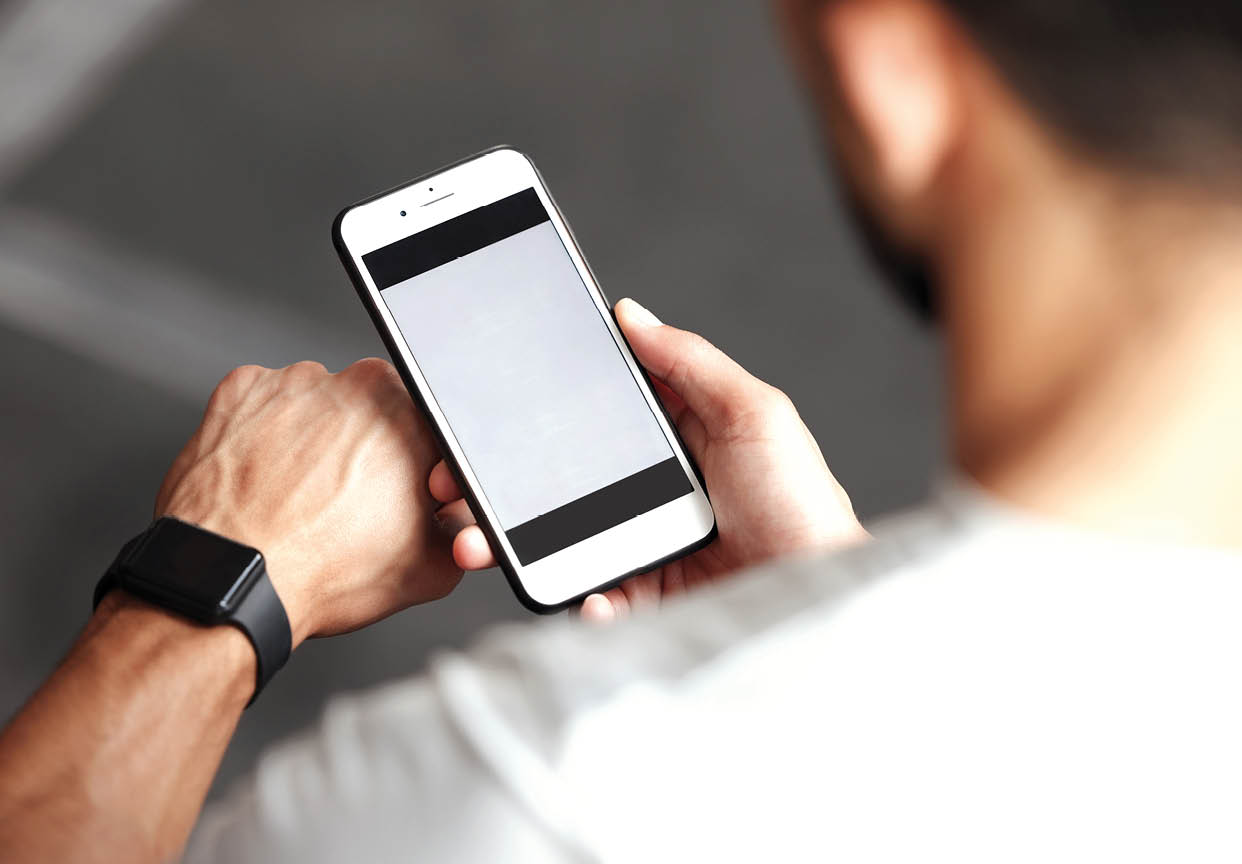 Closeup of one mixed race man checking health applications on digital wristwatch and cellphone for exercise in a gym. Guy from above wearing fitness tracker on arm and reading data about heart rate, body temperature and blood pressure on a phone screen