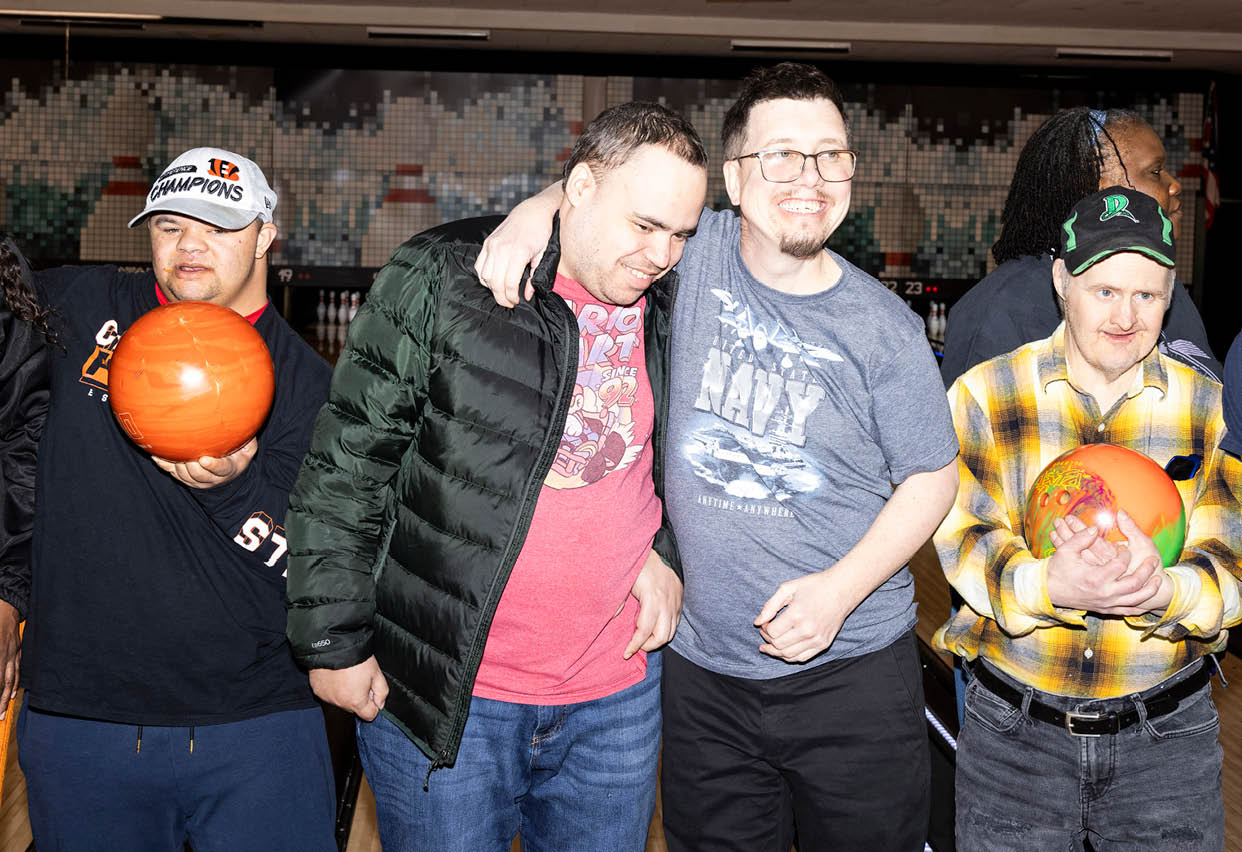 Four men are standing in a line, holding bowling balls. They are wearing black jackets and glasses. AI generated content