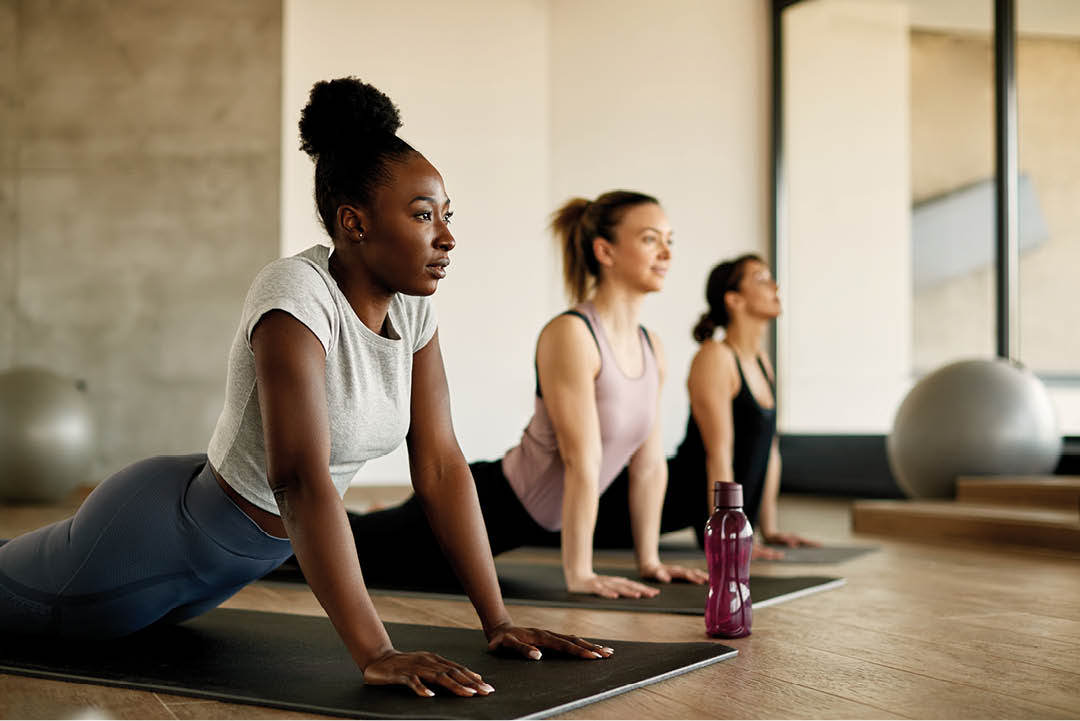 Three women are doing yoga in a room. One woman is on her stomach, another is on her back, and the third is on her knees. They are all holding water bottles. AI generated content