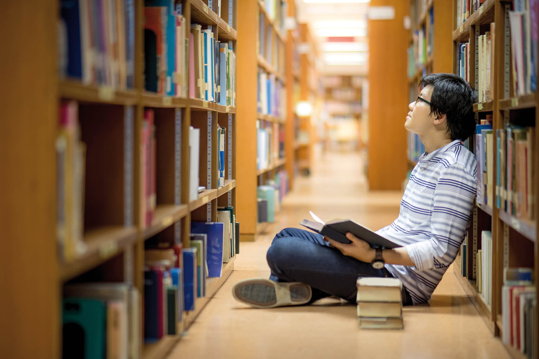 Young Asian man university student reading book in library, education research and self learning in university life concepts