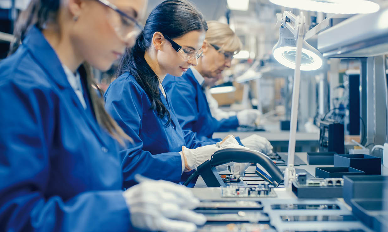 Female Electronics Factory Workers in Blue Work Coat and Protective Glasses Assembling Printed Circuit Boards for Smartphones with Tweezers. High Tech Factory with Employees.