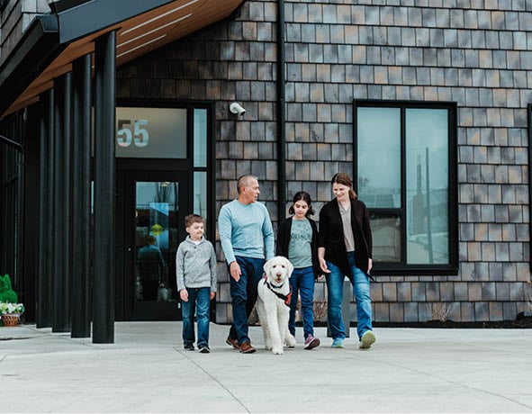A group of people and a dog are standing outside a building. Description generated by AI