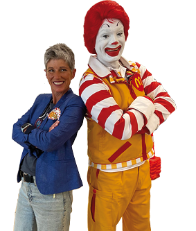 A woman and a Ronald McDonald costume pose for a picture. Description generated by AI