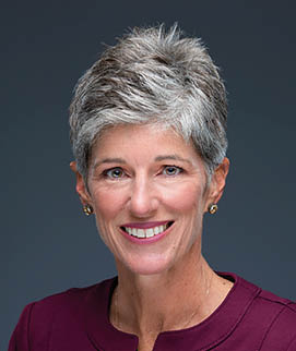 A woman wearing a purple shirt and a necklace. Description generated by AI