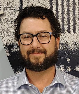 A man wearing glasses and a blue shirt. Description generated by AI