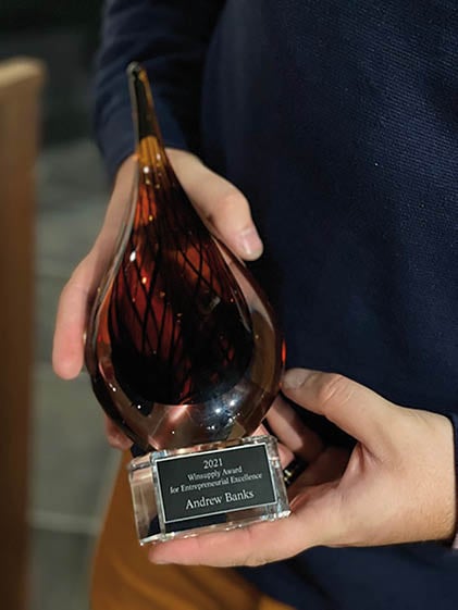 A man holding a glass trophy with the name Andrew Banks on it. Description generated by AI