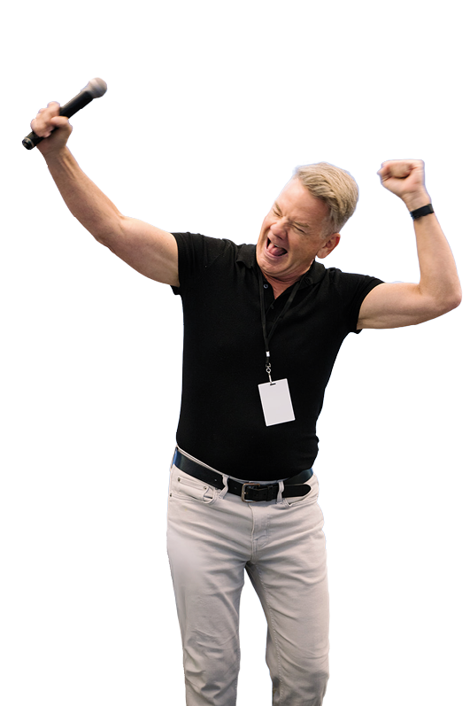 A man wearing a black shirt and white pants is standing in front of a microphone. Description generated by AI