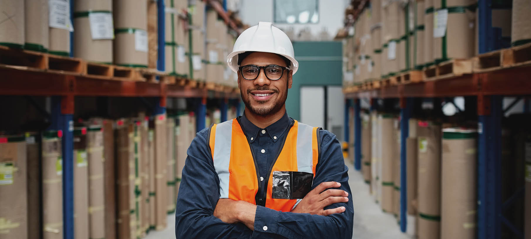 Happy manager in warehouse standing looking at camera with folded hands in a factory