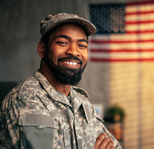 A portrait of a young adult African American army officer inside with the American flag in the background, copy space and looking at camera.