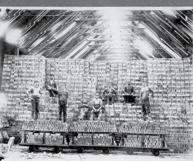 Workers at the National Brick Company. The man seated first in the first row is Wal D. Johnston. The men are sitting and standing on a huge stack of bricks. 