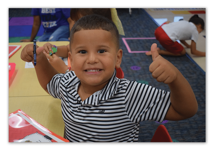 A young boy is sitting at a table, smiling and giving a thumbs up. AI generated content