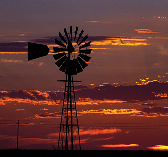 A windmill stands tall in front of a beautiful sunset. AI generated content