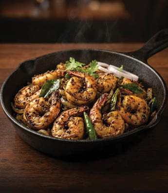 A black skillet filled with shrimp and vegetables sits on a wooden table. AI generated content