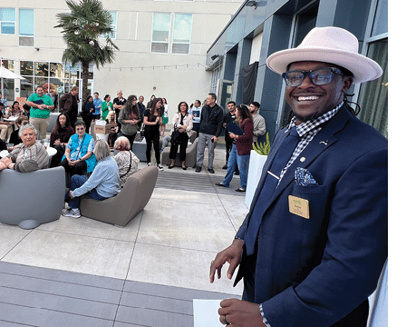 A man in a suit stands on a patio with a crowd of people around him. AI generated content