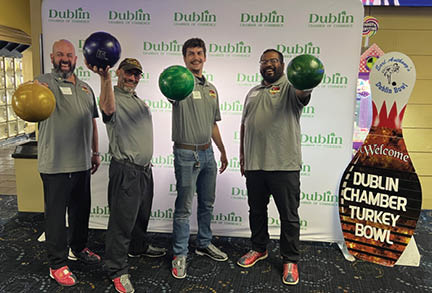 Four men pose with bowling balls in front of a green and white banner. AI generated content