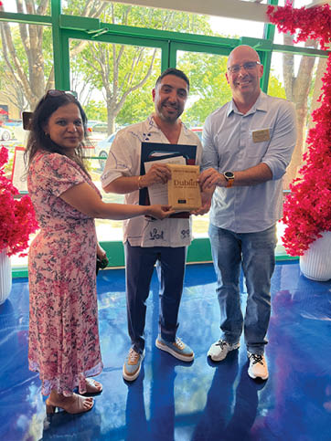 Three people are standing in front of a blue carpet. One man is holding a framed award, and the other two are posing for a picture. AI generated content