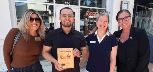 Four people are standing outside a building, posing for a picture. They are all smiling and appear to be enjoying the moment. One of the women is holding a book. AI generated content