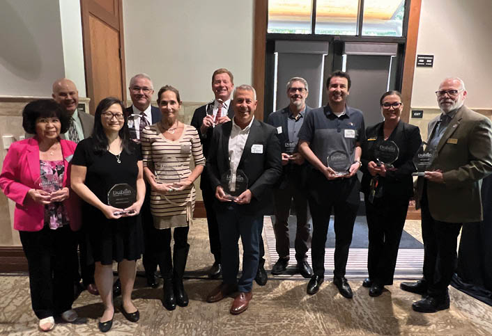 A group of people are standing on a stage, posing for a picture. They are wearing name tags and holding awards. AI generated content