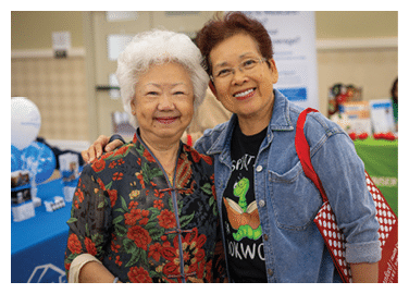 Two women are posing for a picture, one is wearing a floral print shirt and the other is wearing a black shirt. They are both smiling and holding red bags. AI generated content