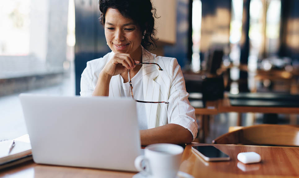 Focused businesswoman working remotely at a cafe, using a laptop with coffee and smartphone on the table. Freelance and creative work environment.