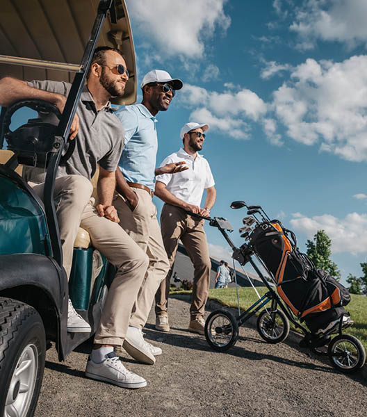 group of smiling friends standing near golf cart and looking away